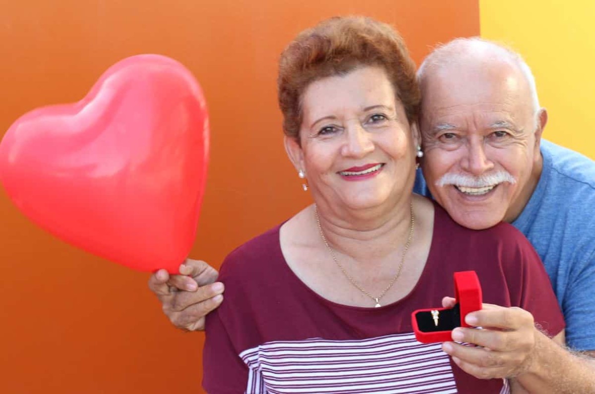 Couple senior souriant tenant un ballon en forme de cœur et un écrin de bijou, symbole d’amour et de complicité pour leurs 46 ans de mariage, les noces de lavande.